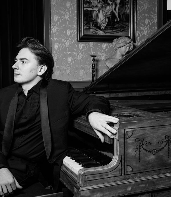 Greg Niemczuk in black and white sitting next to a piano