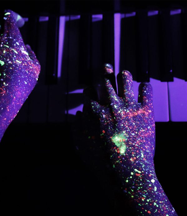 Hands with neon paint playing piano.