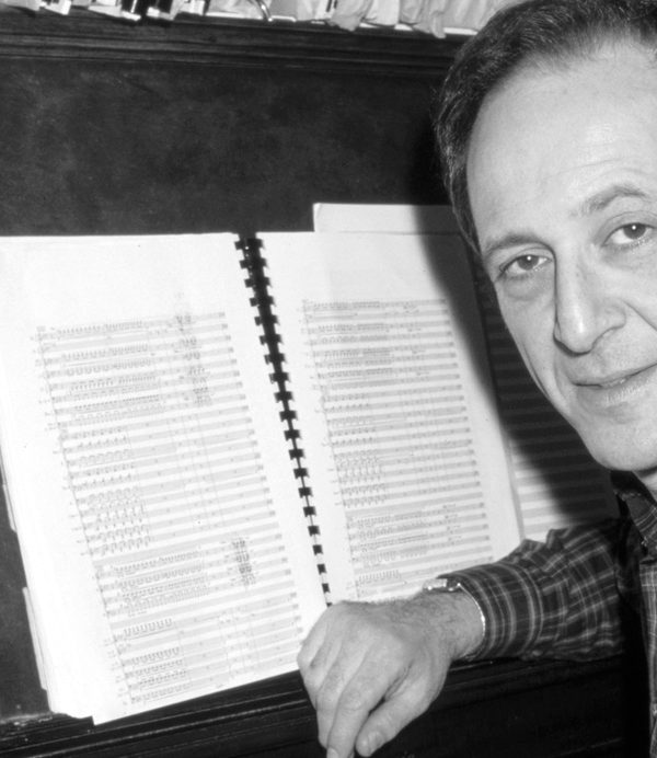 Steve Reich sat at a piano looking to camera.