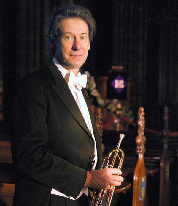 John Wallace holds a trumpet, smiling to camera.