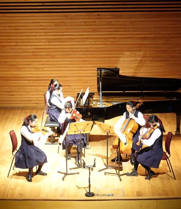 five female students in uniform playing sting quartet and piano