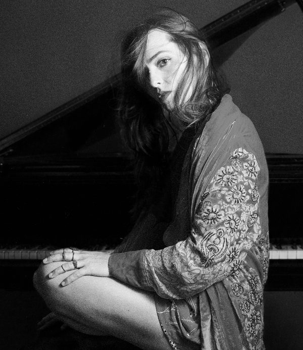 Sarah Coponat looking at camera sitting at a piano