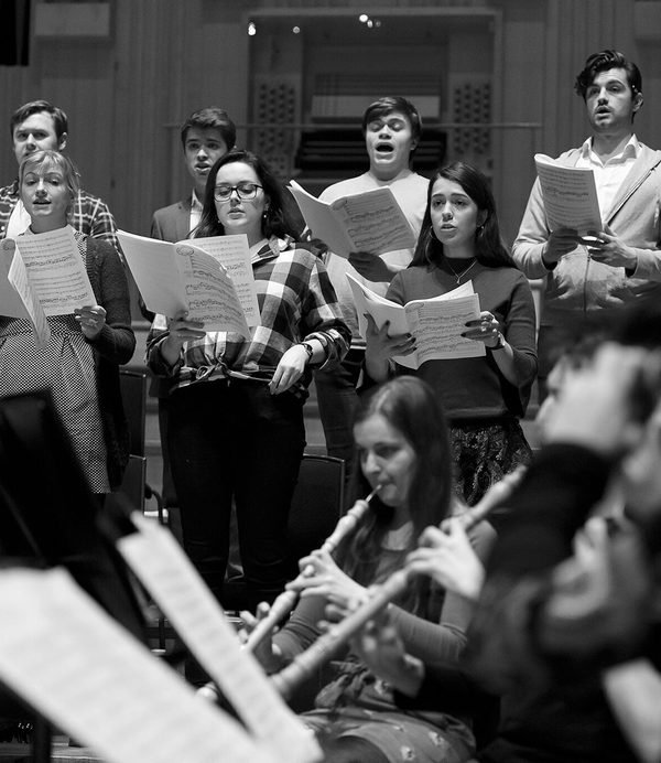 A choir singing in the background, with the orchestra’s brass section blurred in the foreground.