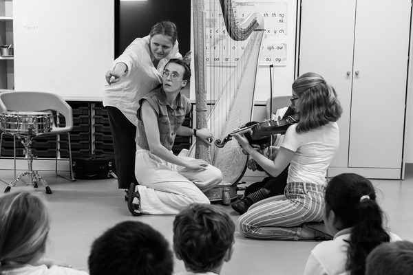 A harpist and violinist perform in front of children.