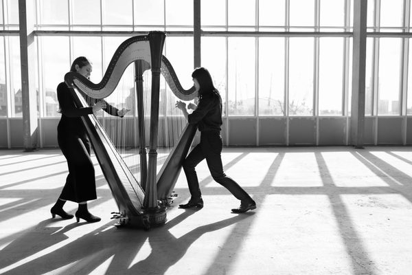 Two harpists play standing up, facing each other.