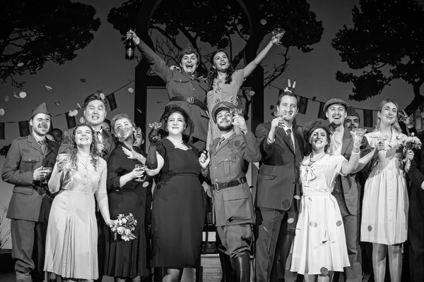 An operatic ensemble in concert smiling to audience triumphantly.