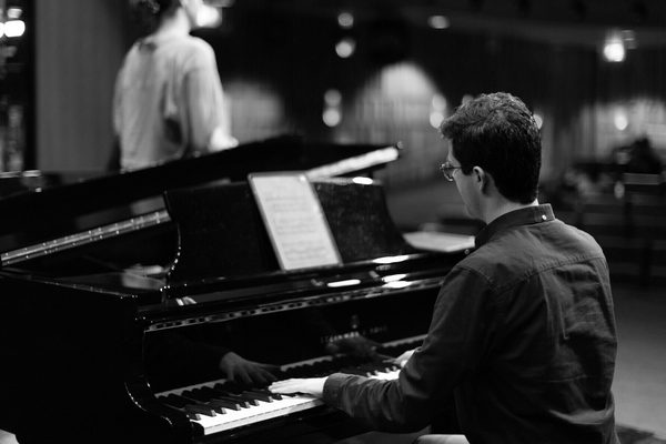 A pianist an vocalist on stage, viewed from behind.