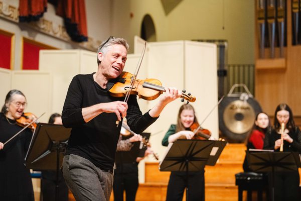 Bjarte Eike plays the violin on stage, surrounded by Academy students