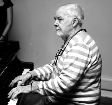 A portrait of George Hall sat at the piano