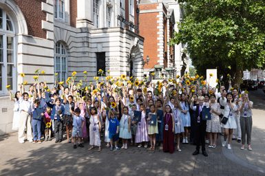 Participants in the New Talent Festival 2026 hold sunflowers above their heads in front of the facade of the Royal Academy of Music