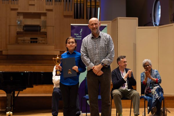 John Hutchins stands next to the Royal Academy of Music Prize winner on stage in front of a grand piano