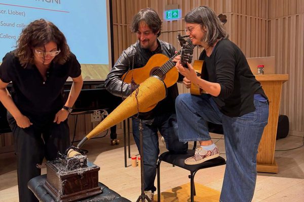 Three musicians recording a guitar with a phonograph.