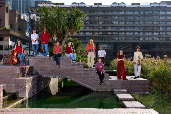 Musicians stand on a bridge over a river