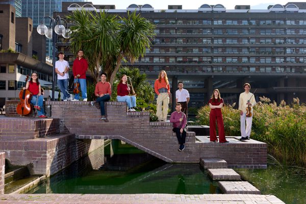 Musicians stand on a bridge over a river