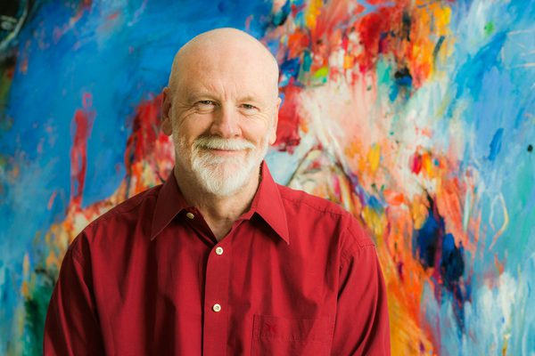 Brett Dean stands against a colourful artwork