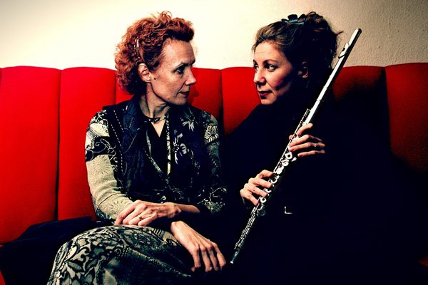Kaija Saariaho with Camilla Hoitenga are sat on a red sofa