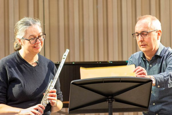 David Gorton and Dr Carla Rees are sat behind a music stand. David holds music and Carla holds a flute.