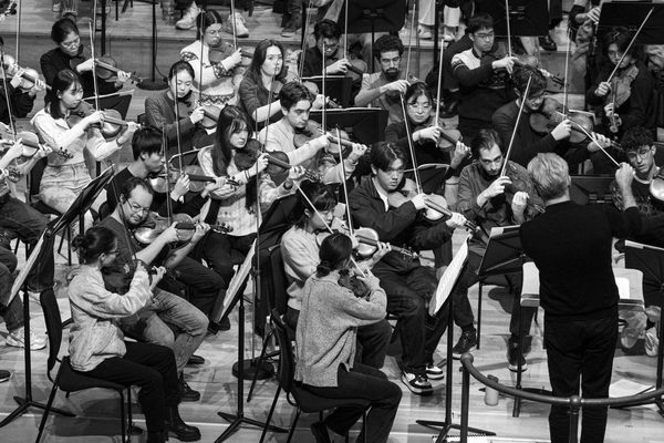 A conductor dressed in black conducts an orchestra on stage
