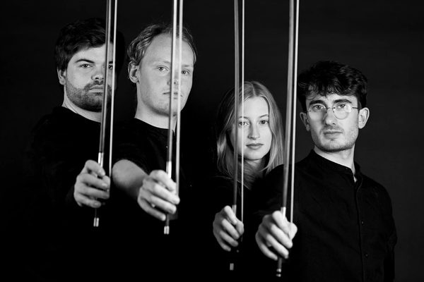 An image of the four members of the Fibonacci Quartet: Kryštof Kohout, Luna De Mol, Elliot Kempton and Findlay Spence, looking at the camera and holding their bows out in front of them