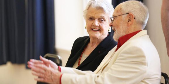 George Hall and Angela Lansbury are sat down chatting. They are both smiling.
