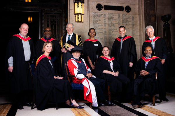 10 people pose for a photo in graduation attire.