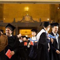 Image of students wearing ceremonial gowns and mortarboards at the 2025 Graduation Ceremony, hugging, smiling and talking.