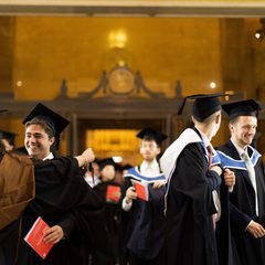 Image of students wearing ceremonial gowns and mortarboards at the 2025 Graduation Ceremony, hugging, smiling and talking.