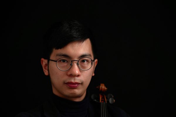 An image of Joe Chu Yu Yang looking into the camera, holding a violin