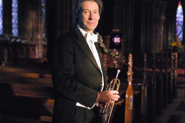 John Wallace stands in a church, holding a trumpet.