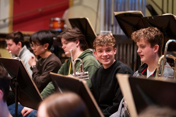 Junior Academy students holding woodwind instruments sit behind music stands
