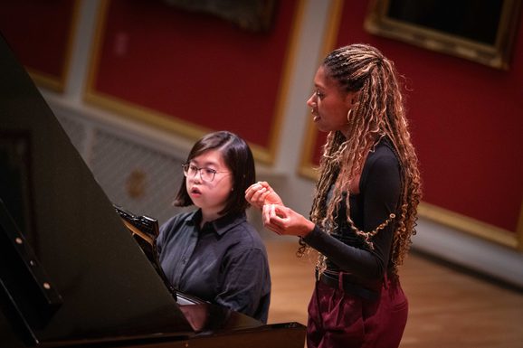 Isata Kanneh Mason speaks with a Junior Academy student, next to a grand piano