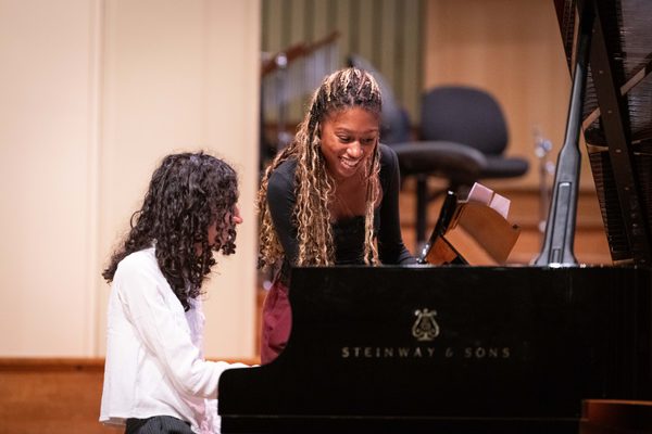 Isata Kanneh Mason speaks with a Junior Academy student, next to a grand piano