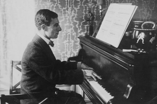 Black and white image of Maurice Ravel sitting at a piano