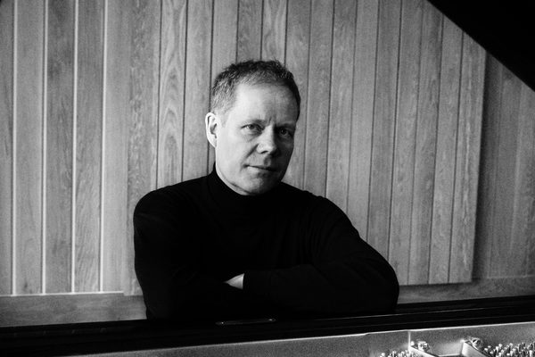 Max Richter sits at a piano, against a wooden wall