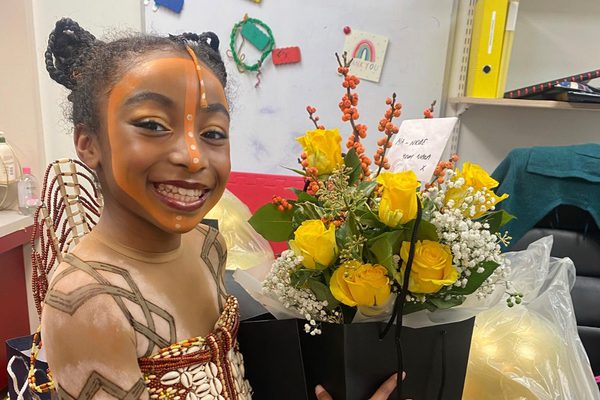 Mia-Nicole Alexander in costume as 'Young Nala' for The Lion King, pictured smiling and holding a bouquet of flowers