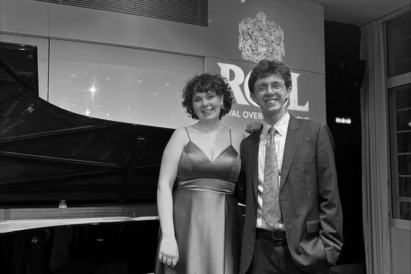 Klara Solen and George Herbert stand on the ROSL stage in front of a piano