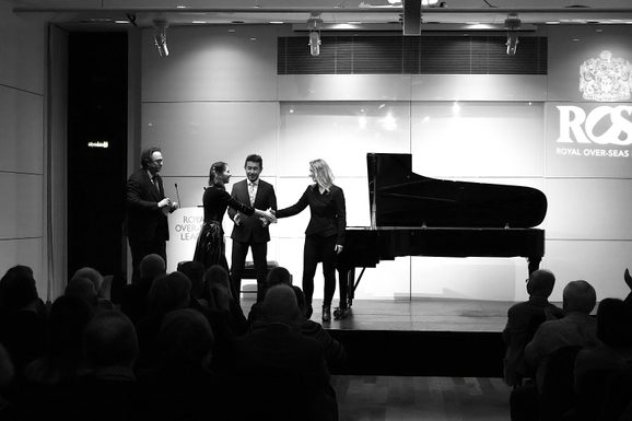 Finalists stand on the ROSL stage in front of a piano. Two people shake hands