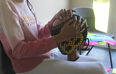 A seated girl playing a beaded percussion instrument