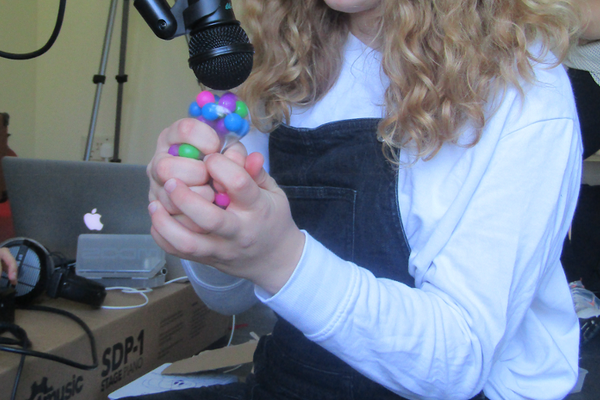 A girl making sounds into a microphone with plastic beads in her hands