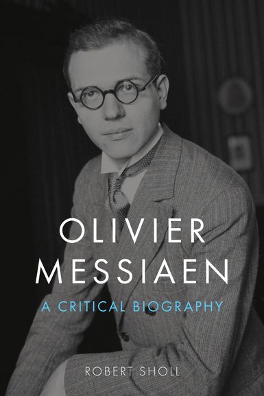A man with round framed glasses, sitting in profile looking at the camera, wearing a jacket, shirt and cravat