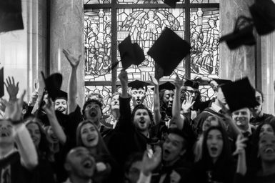 A black and white image of graduates throwing their caps in the air