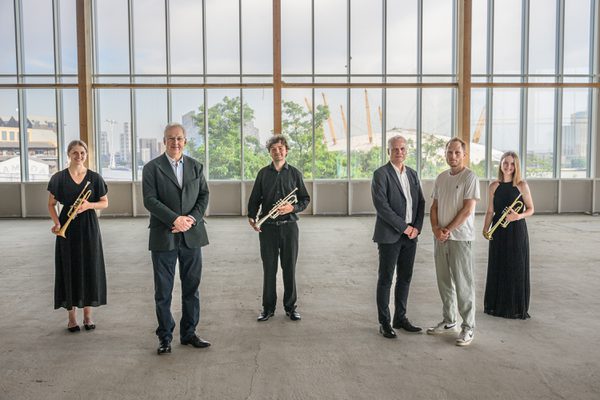 Brass students pose for photo with professors in open plan room.