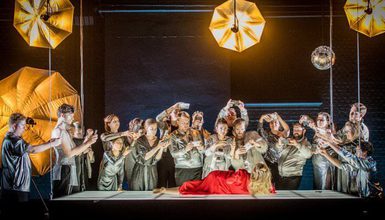 Scene from the opera Semele. A lady lays wearing a red gown. A group surrounds her taking photos