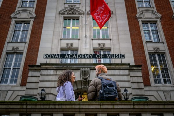 Two students stand outside of the Royal Academy of Music. The facade of the building can be seen in the background