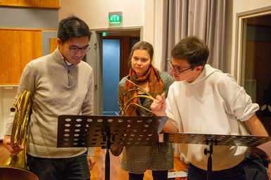 Three music students grouped around a music stand with their instruments