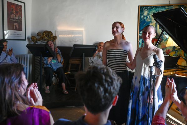 Milda Daunoraitė and Abigail Sinclair standing in front of a piano, receiving an ovation from an audience in a small room