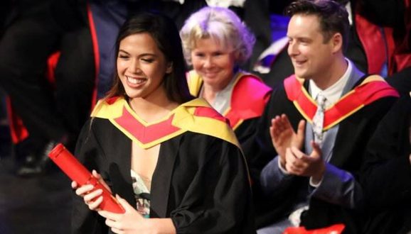 Student receives a graduation certificate. Imelda Staunton can be seen sat behind the student.