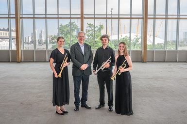 A brass ensemble pose for a photo in an open-plan building.