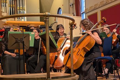 Cellist Mayuchi Ono on stage in the Duke's Hall as part of the Junior Academy Symphony Orchestra, pictured smiling