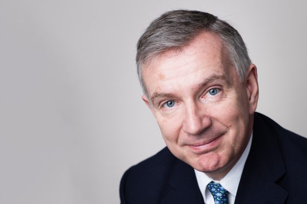 Sir Simon Robey smiles for camera against a grey backdrop